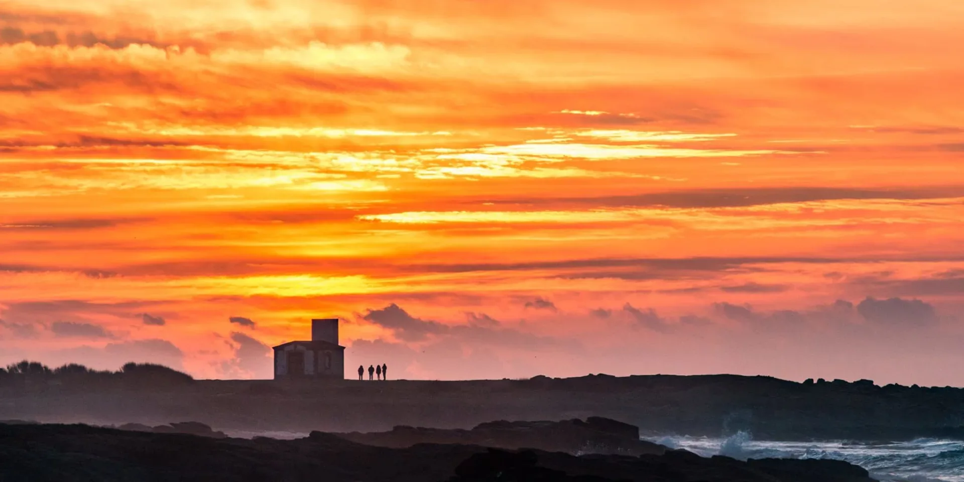 Coucher de soleil flamboyant sur la côte sauvage de l'Île d'Yeu avec silhouettes de promeneurs près d'une tour historique