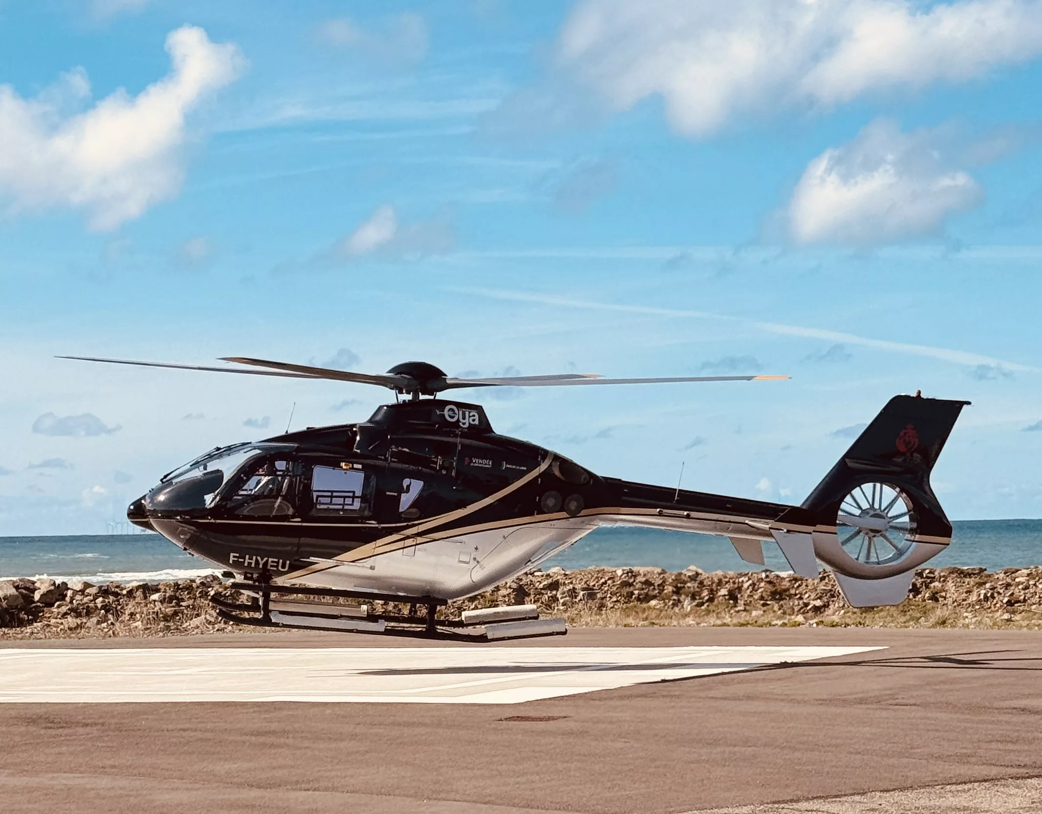 Hélicoptère noir de luxe Oya posé sur l'héliport de l'Île d'Yeu avec vue sur l'océan Atlantique en arrière-plan