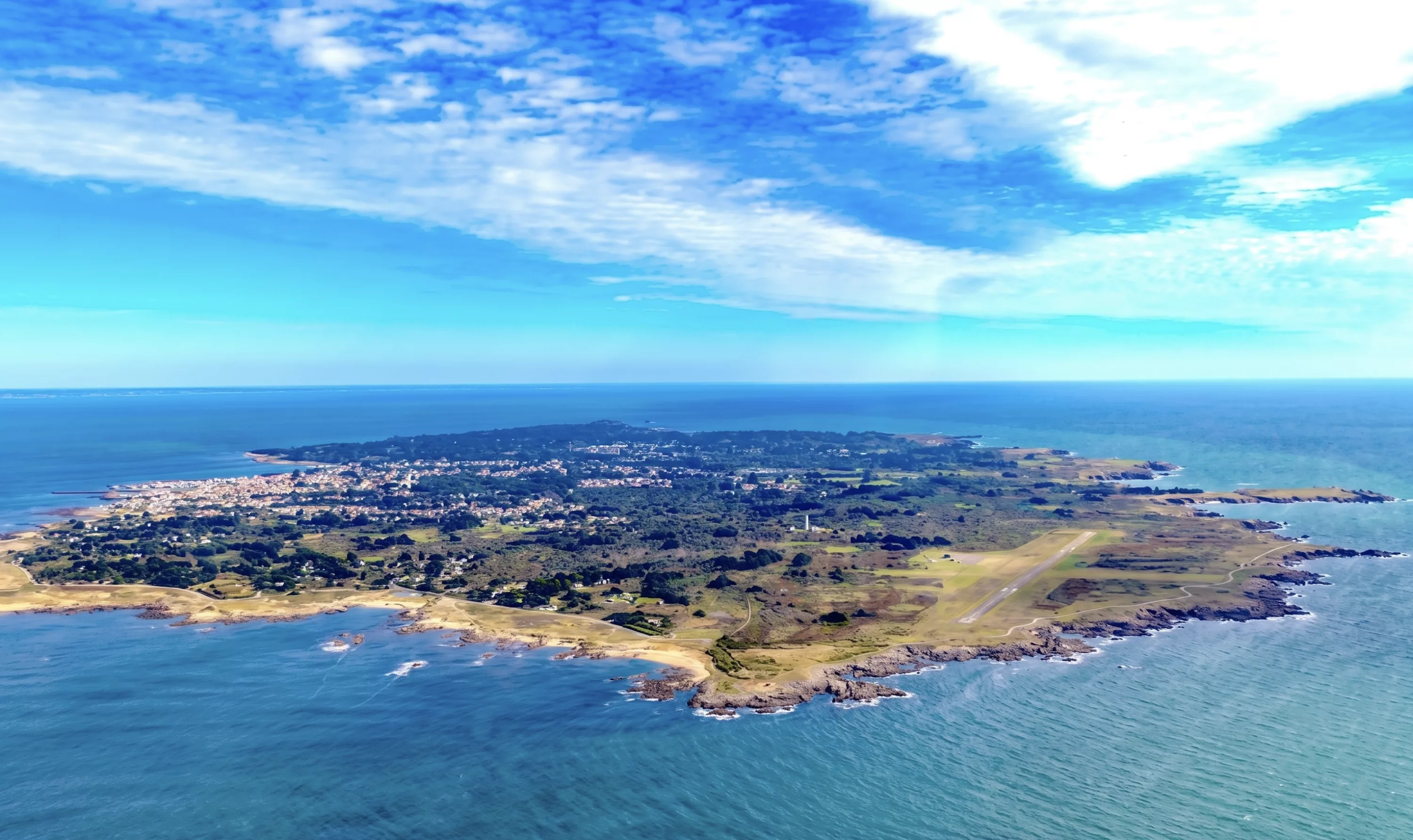 Vue aérienne panoramique de l'Île d'Yeu en Vendée avec ses côtes rocheuses, ses plages et son océan turquoise sous un ciel bleu